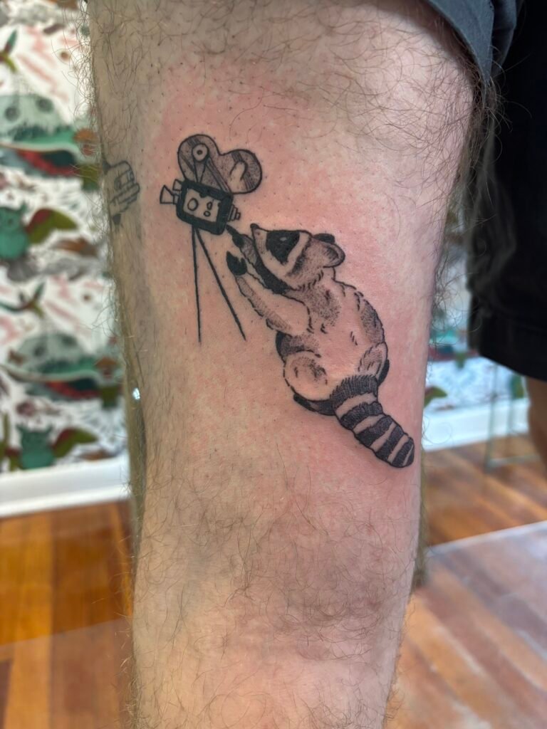 raccoon illustration black and grey tattoo with camera on leg